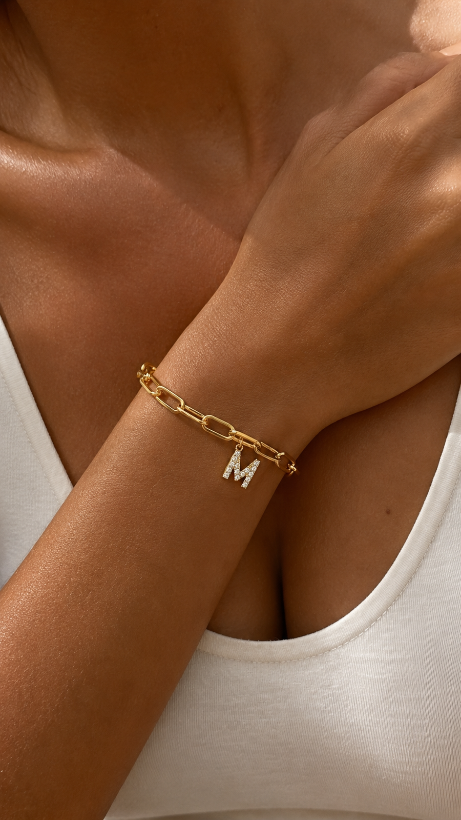 Pulseira dourada personalizada com inicial A, corrente paperclip e pendente de letra cravejado no pulso feminino.
