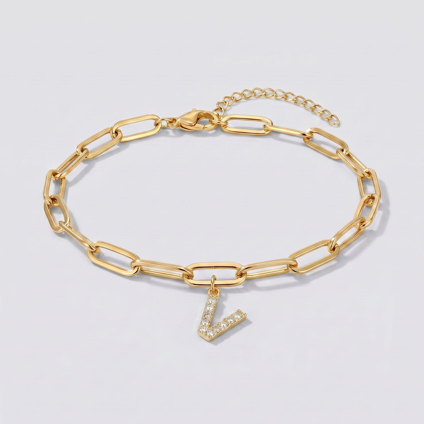 Pulseira dourada com letra inicial V, corrente paperclip e pendente de letra cravejado.