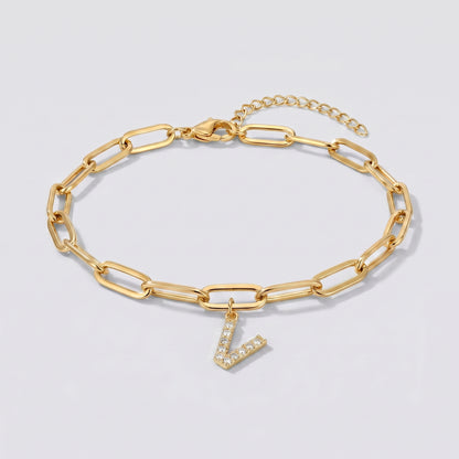 Pulseira dourada com letra inicial V, corrente paperclip e pendente de letra cravejado.
