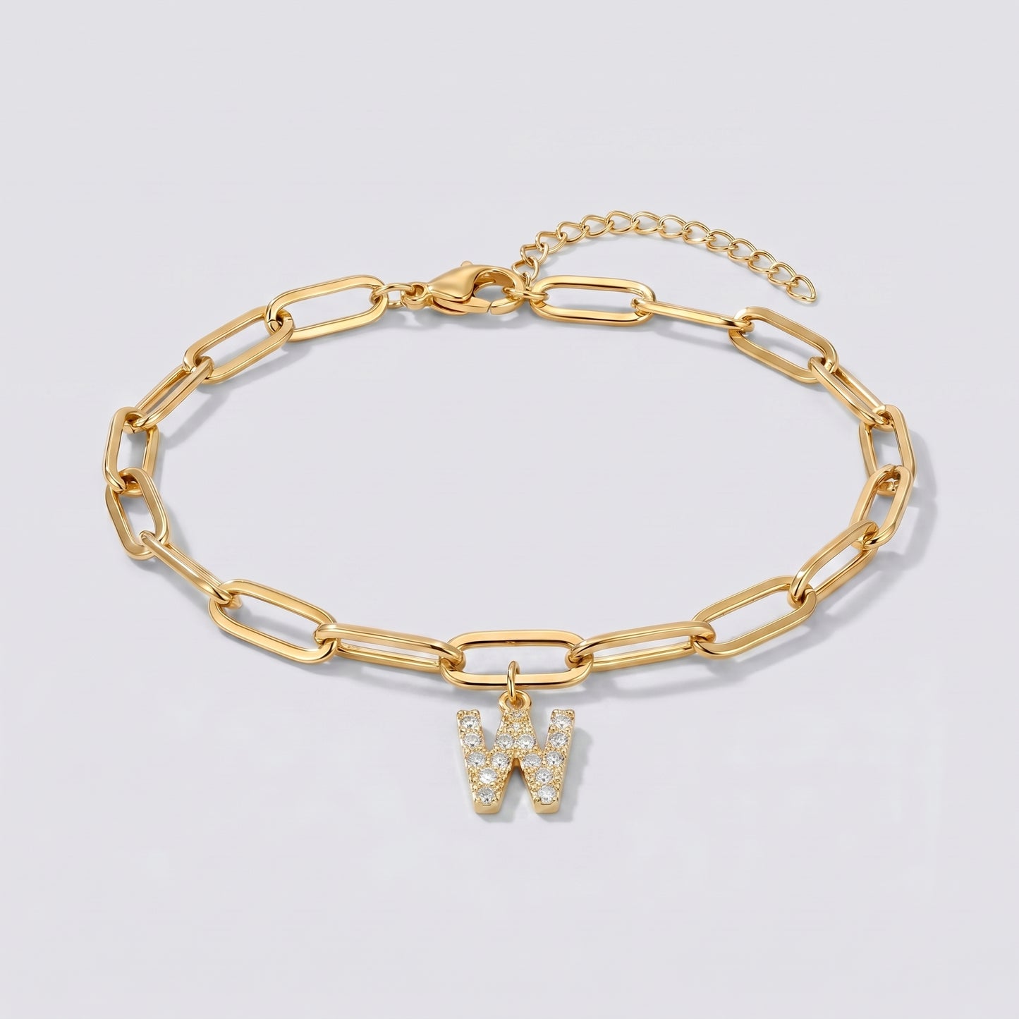 Pulseira dourada com letra inicial W, corrente paperclip e pendente de letra cravejado.