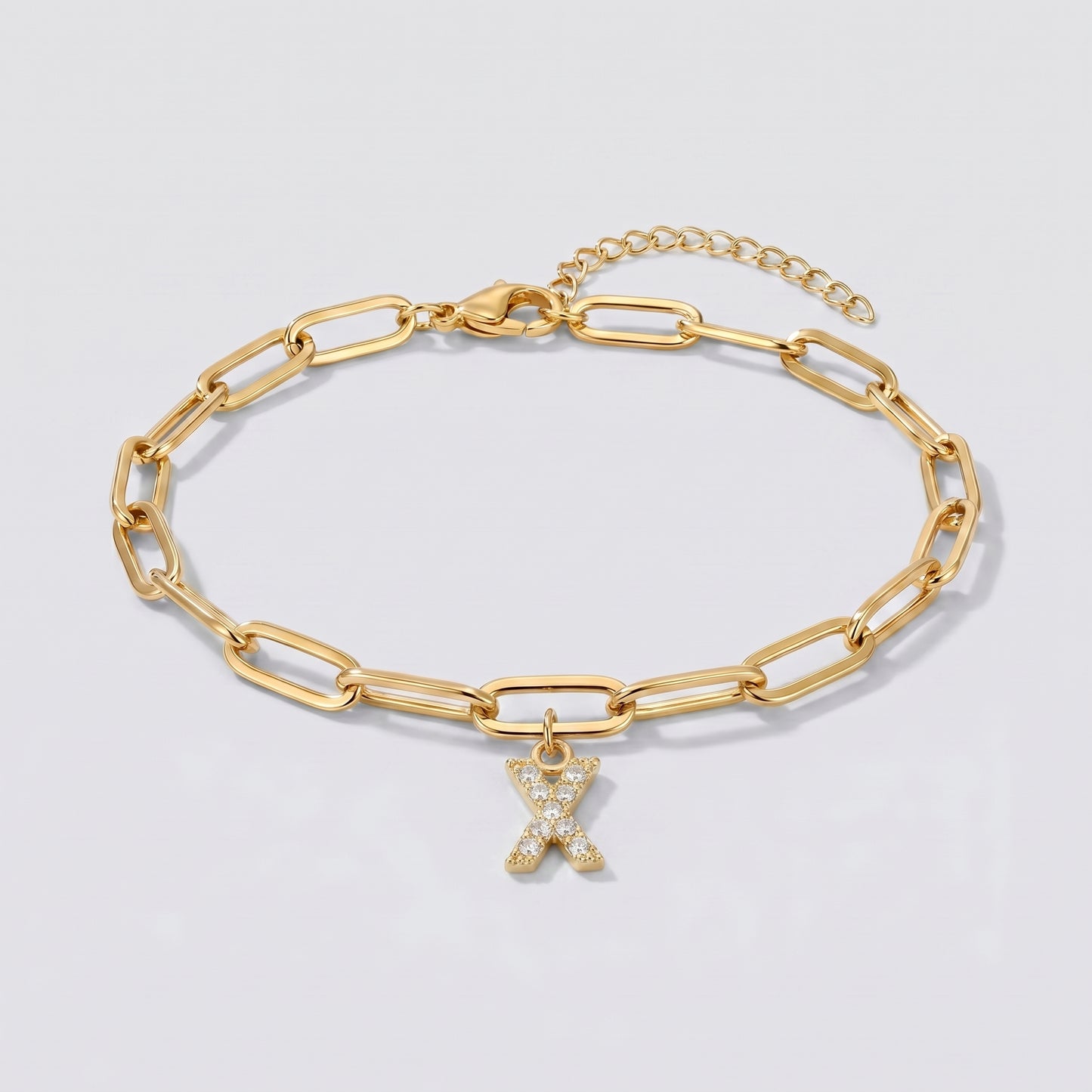 Pulseira dourada com letra inicial X, corrente paperclip e pendente de letra cravejado.