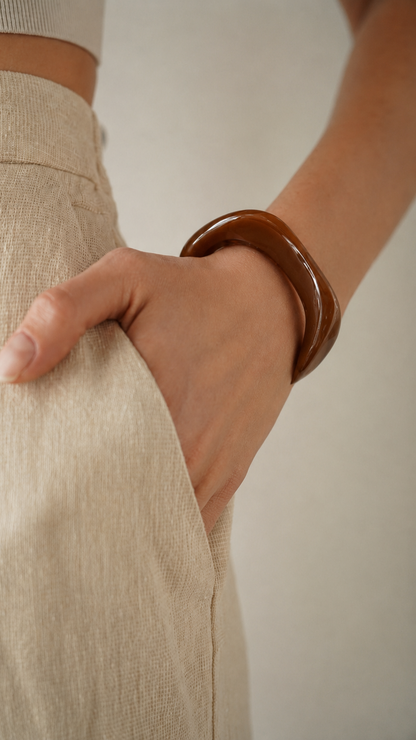 Pulseira de resina castanha usada no pulso, com acabamento brilhante e estilo elegante.