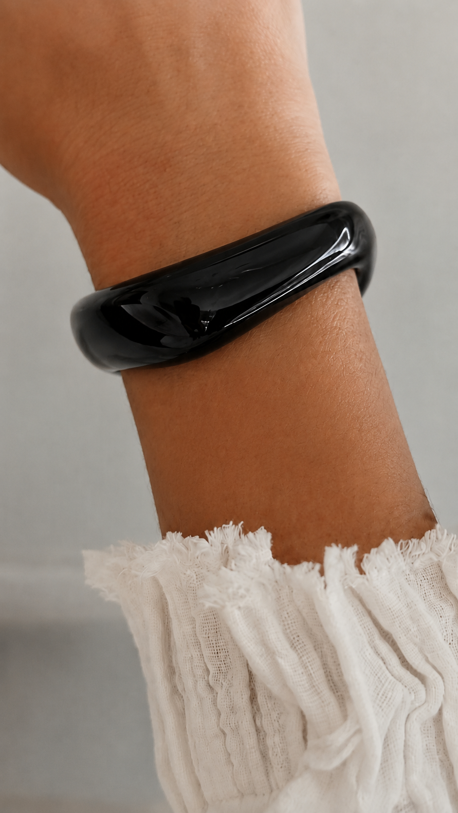 Pulseira de resina preta usada no pulso, com acabamento brilhante e estilo elegante.