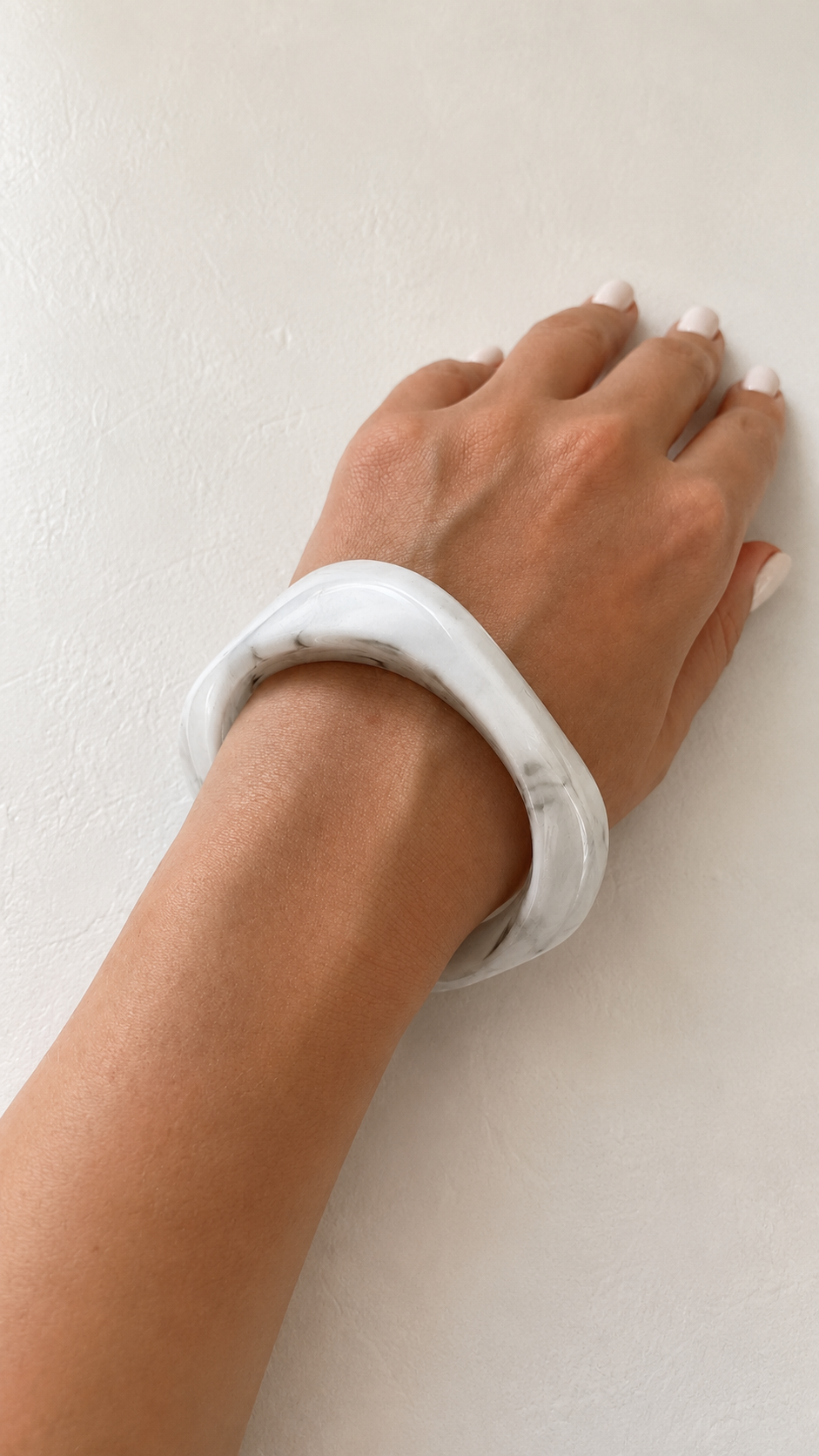 Pulseira de resina branca marmoreada usada no pulso, com acabamento brilhante e estilo elegante.