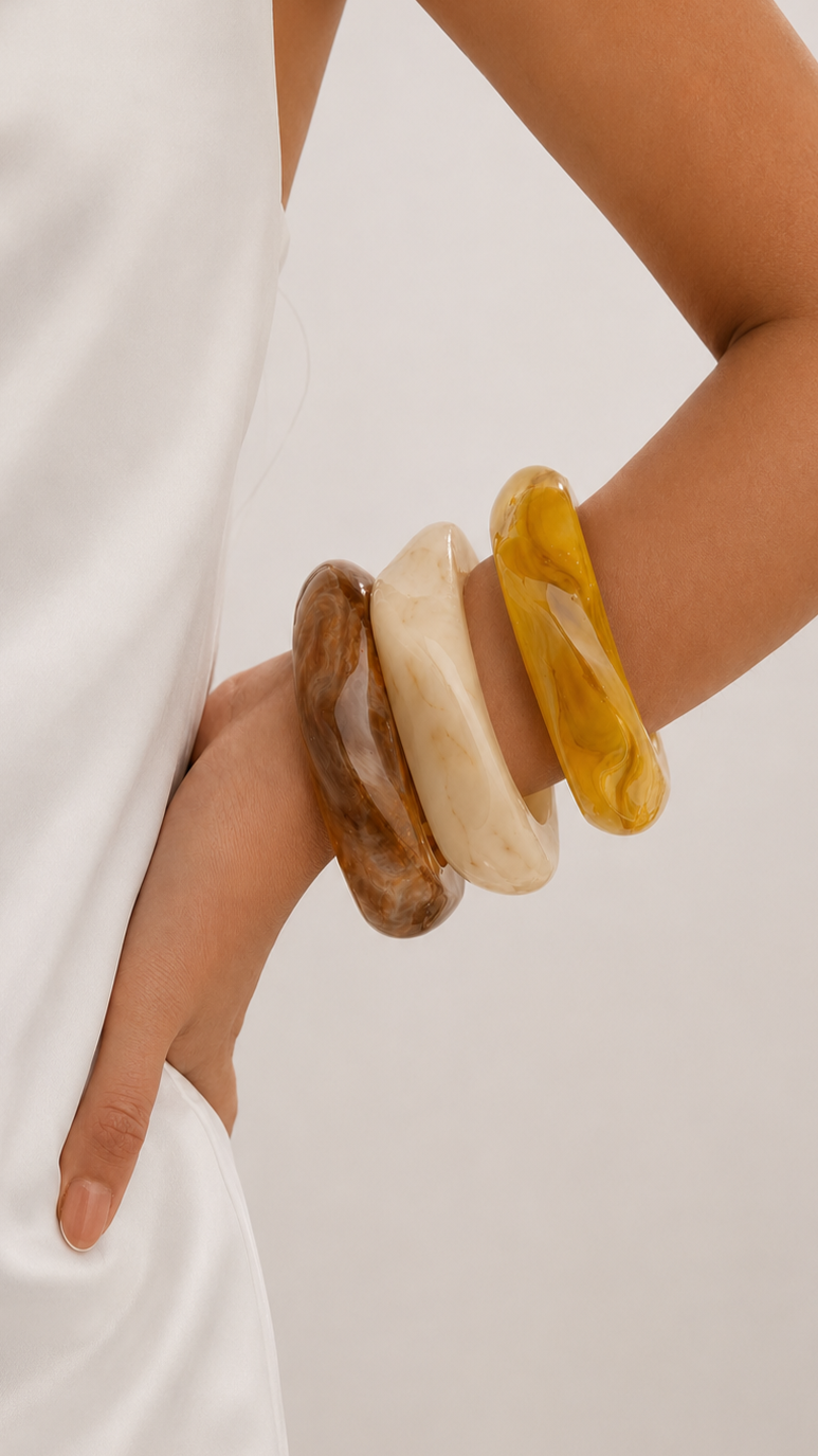 Pulseiras de resina em castanho, bege e amarelo usadas no pulso, com design elegante e acabamento brilhante.