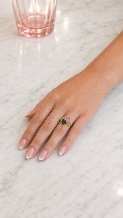 Mulher a usar anel dourado com duas pedras de nascimento — Outubro (Turmalina Rosa, pera) e Maio (Esmeralda, retângulo).