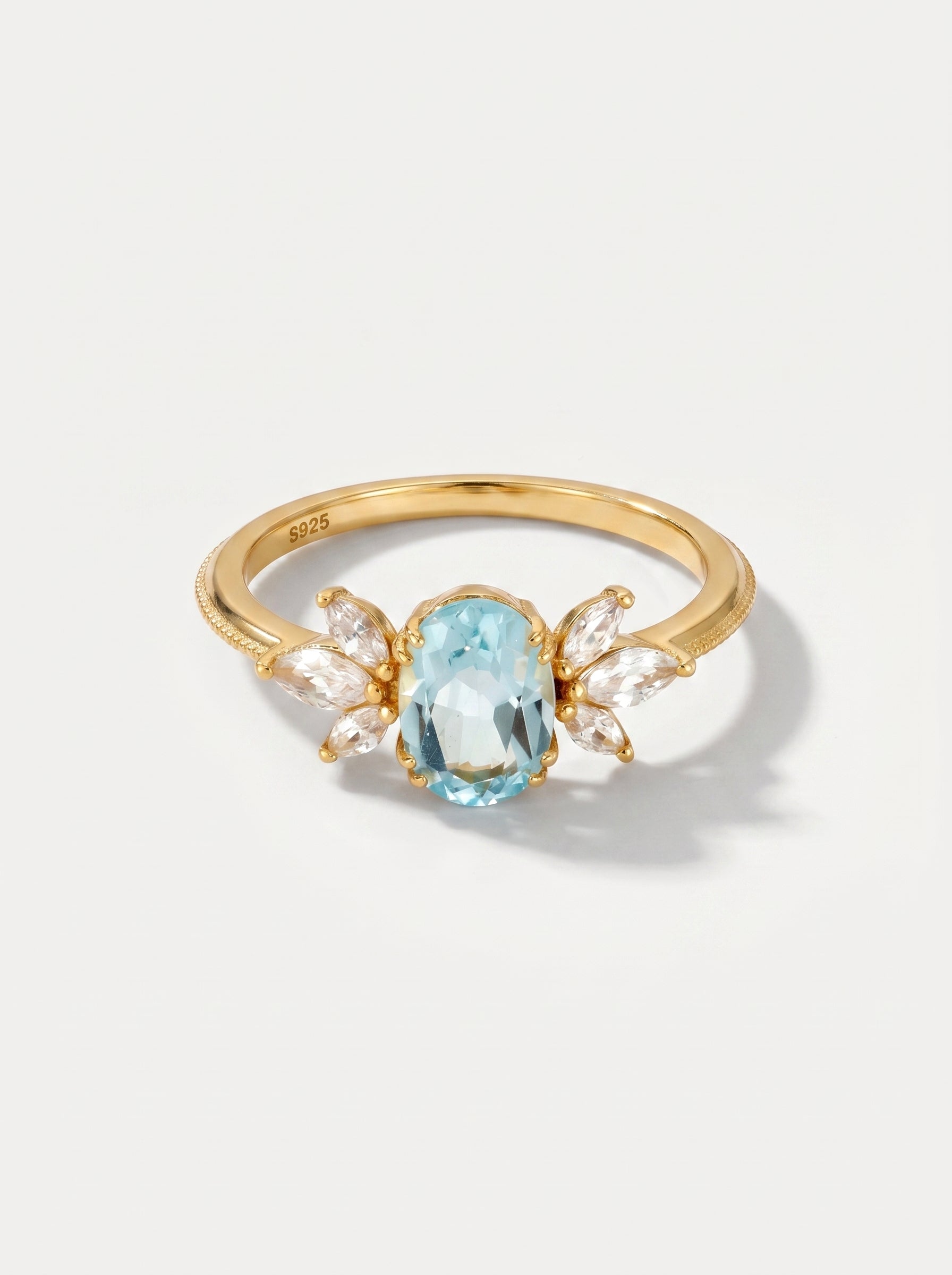 Anel em ouro com uma pedra preciosa azul sobre um fundo cinzento claro.