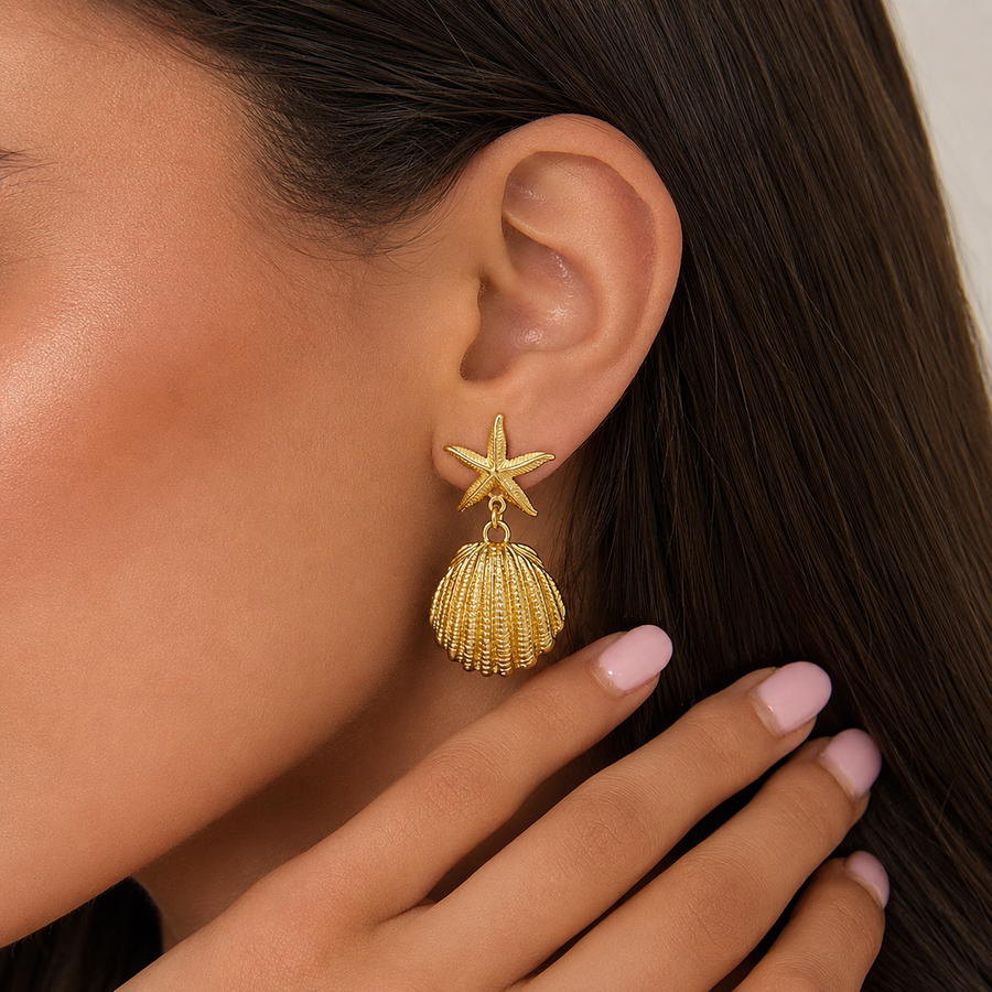 Brincos dourados com estrela-do-mar e pingente de concha usados na orelha, para um visual elegante, feminino e inspirado no mar.