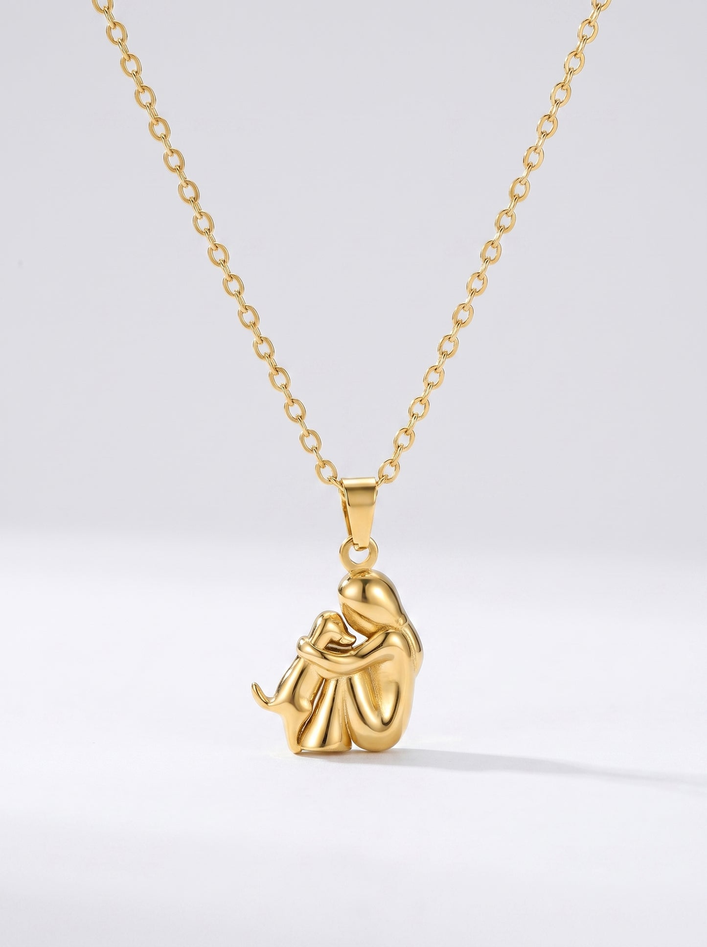 Colar dourado delicado com pendente artístico abstrato e acabamento brilhante, fotografado sobre fundo claro para um visual elegante, moderno e sofisticado.