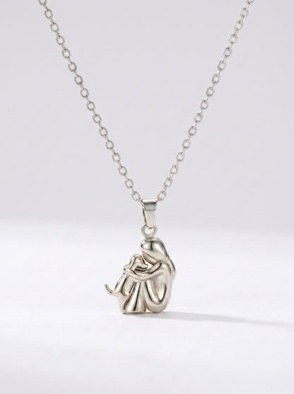 Colar prateado delicado com pendente artístico abstrato e acabamento brilhante, fotografado sobre fundo claro para um visual moderno, elegante e sofisticado.