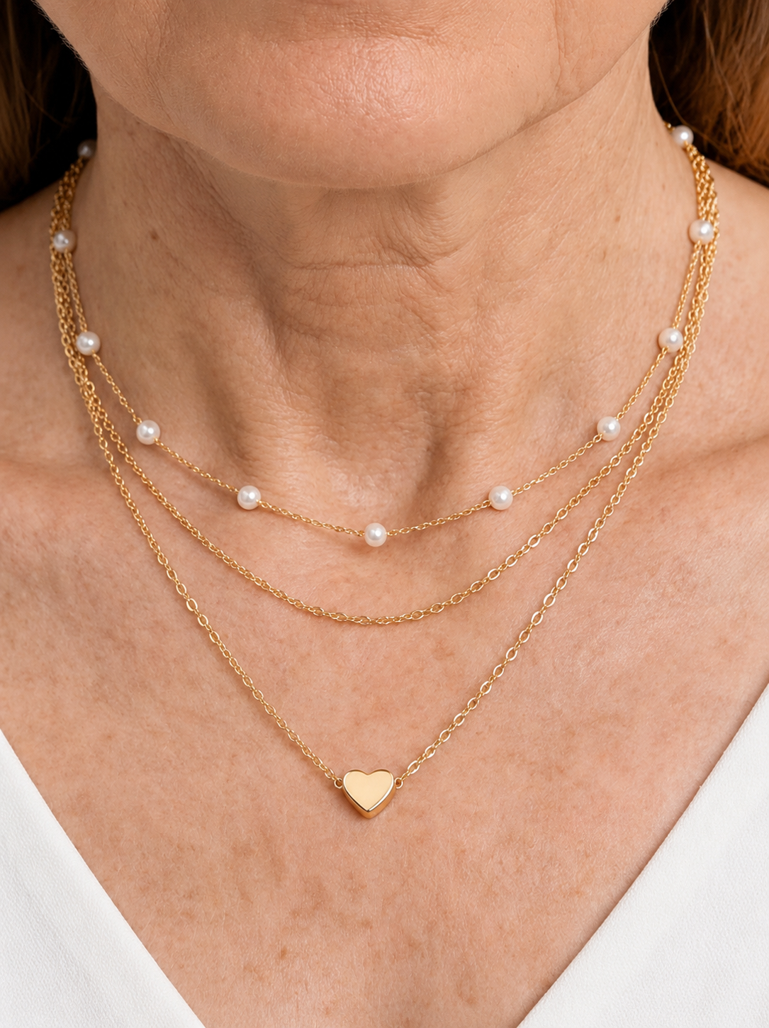 Colar dourado delicado em camadas com pérolas brancas e pendente em forma de coração, usado ao pescoço para um visual elegante, romântico e sofisticado.
