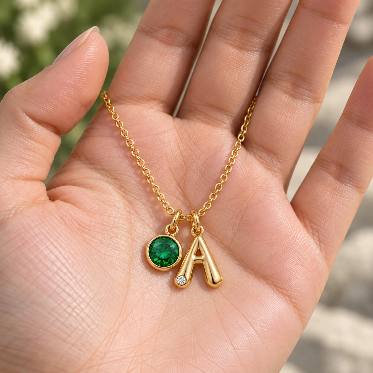 Colar Inicial A dourado com pedra Esmeralda apresentado na mão