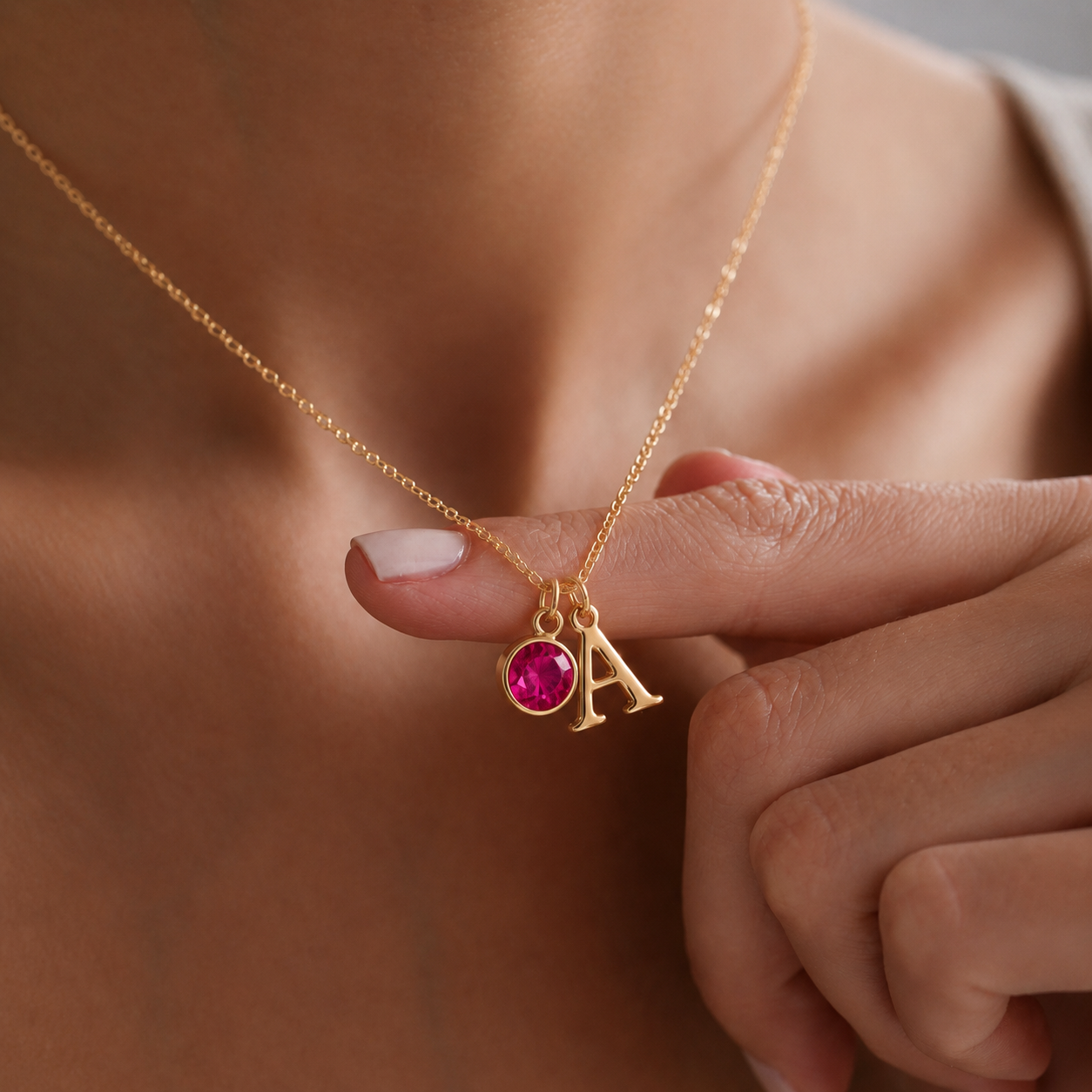 Close-up de colar dourado com inicial A e pedra de nascimento rosa, segurado à mão para destacar os detalhes personalizados.