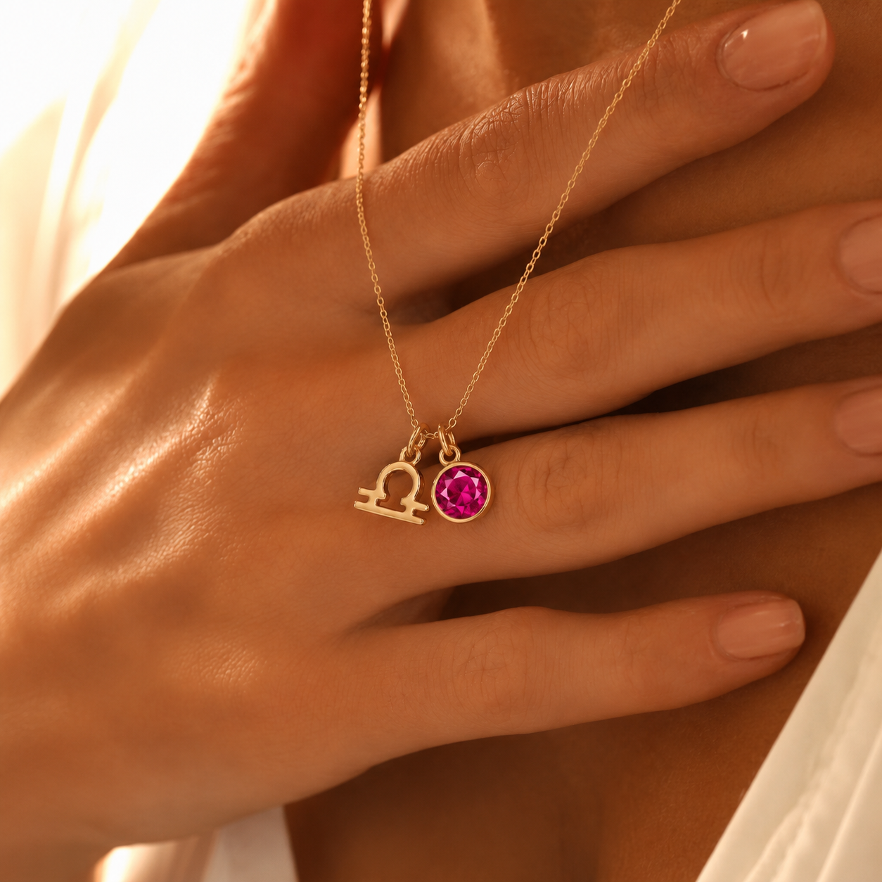 Close-up de colar dourado personalizado com símbolo do signo Balança e pedra de nascimento rosa, segurado sobre o peito.