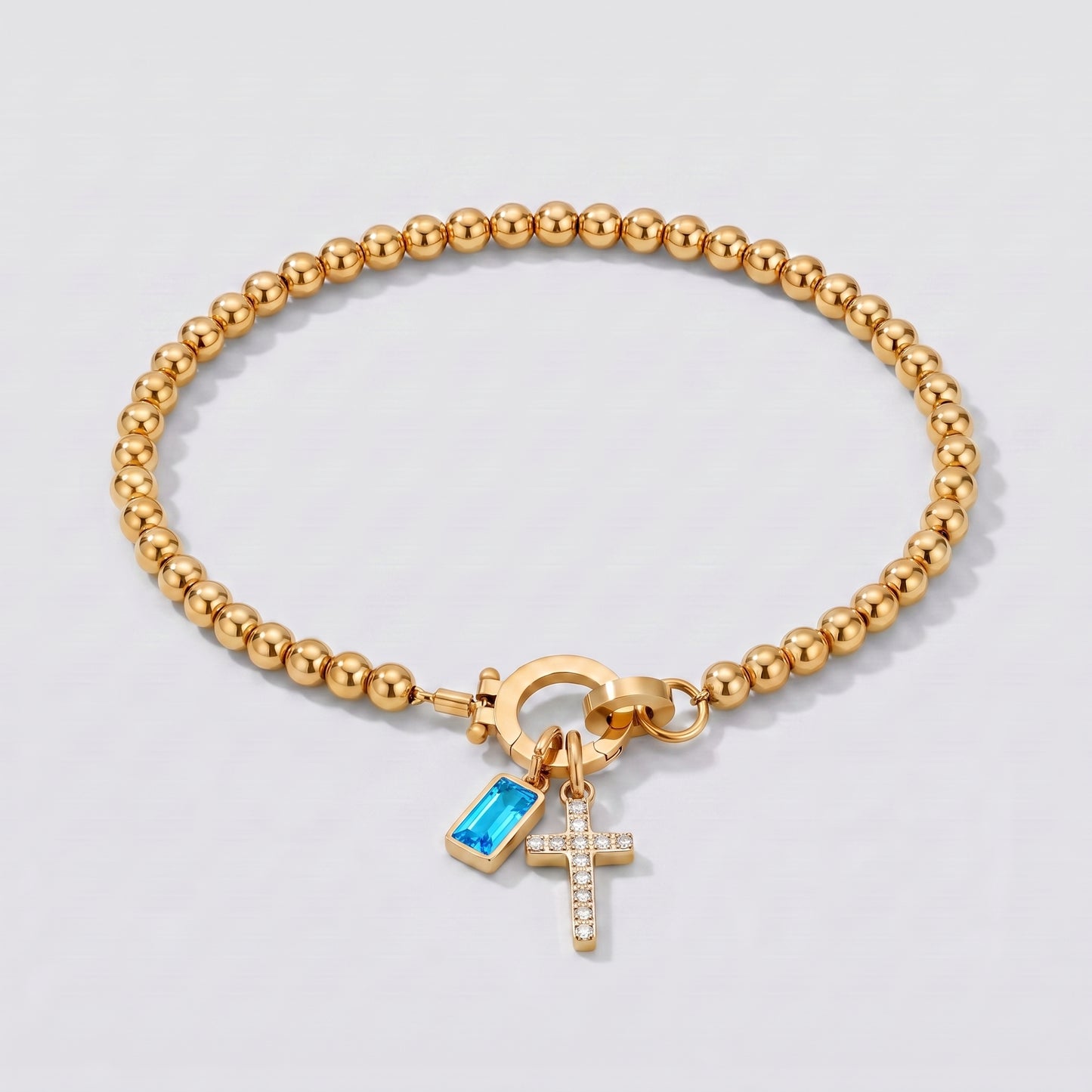 Pulseira dourada de contas com cruz e pedra de nascimento topázio azul de dezembro.