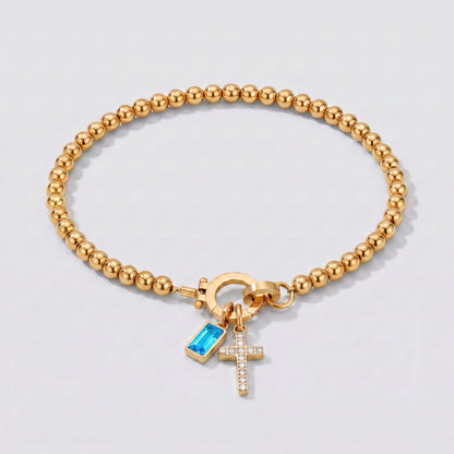 Pulseira dourada de contas com cruz e pedra de nascimento topázio azul de dezembro.