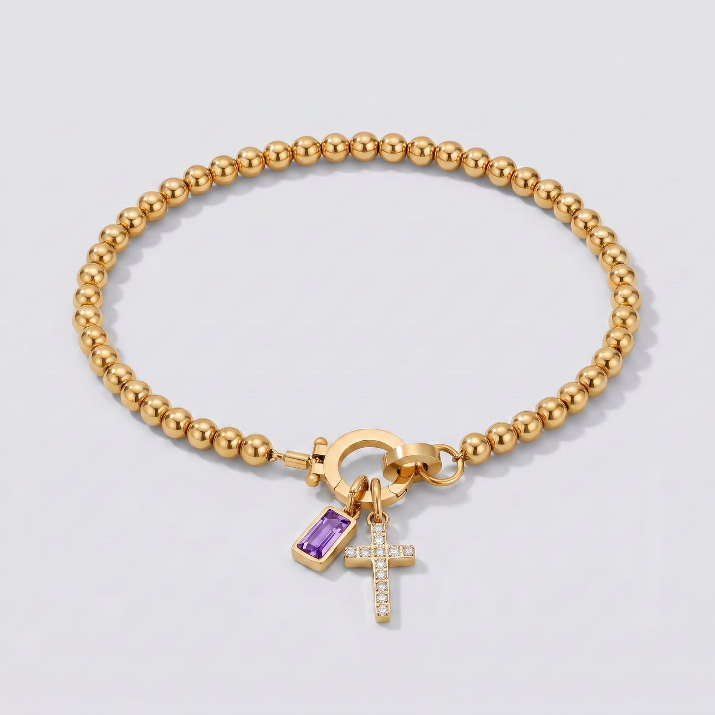 Pulseira dourada de contas com cruz e pedra de nascimento ametista de fevereiro.