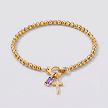 Pulseira dourada de contas com cruz e pedra de nascimento ametista de fevereiro.