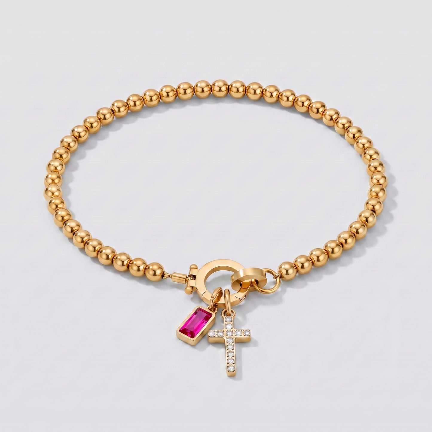 Pulseira dourada de contas com cruz e pedra de nascimento rubi de julho.
