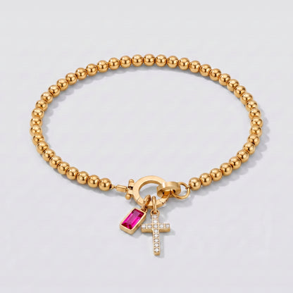 Pulseira dourada de contas com cruz e pedra de nascimento rubi de julho.