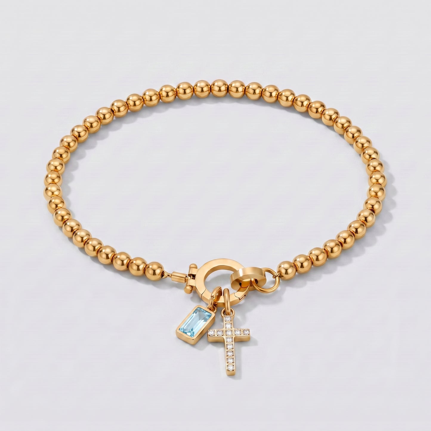 Pulseira dourada de contas com cruz e pedra de nascimento agua marinha de março.