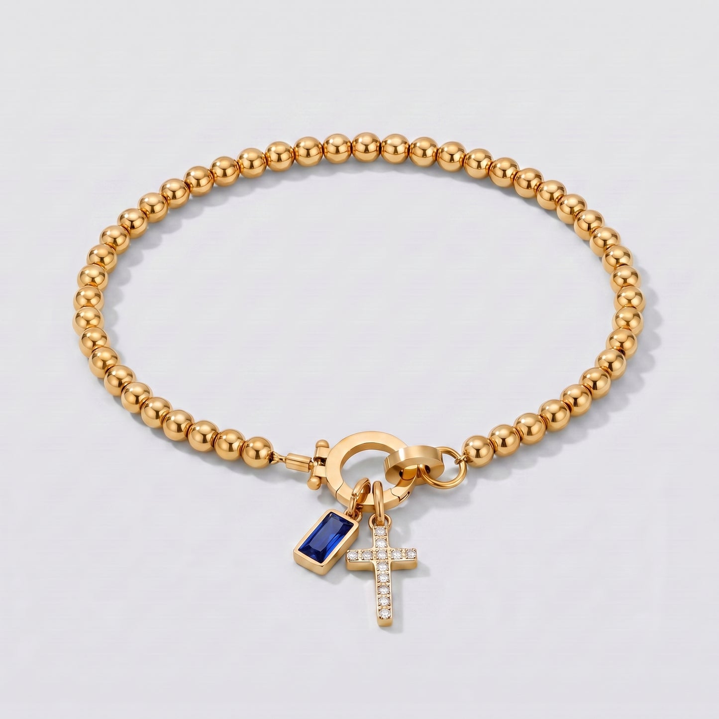 Pulseira dourada de contas com cruz e pedra de nascimento safira azul de setembro.