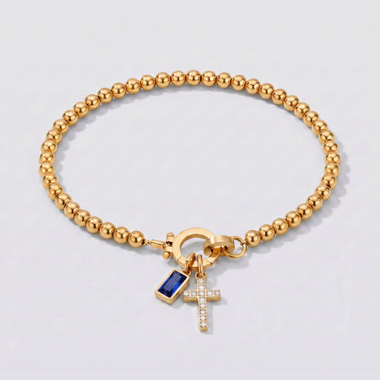 Pulseira dourada de contas com cruz e pedra de nascimento safira azul de setembro.