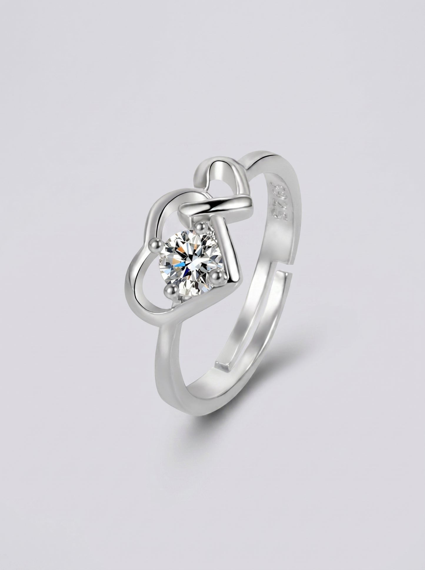 Anel em prata com um diamante em forma de coração sobre um fundo cinzento claro.
