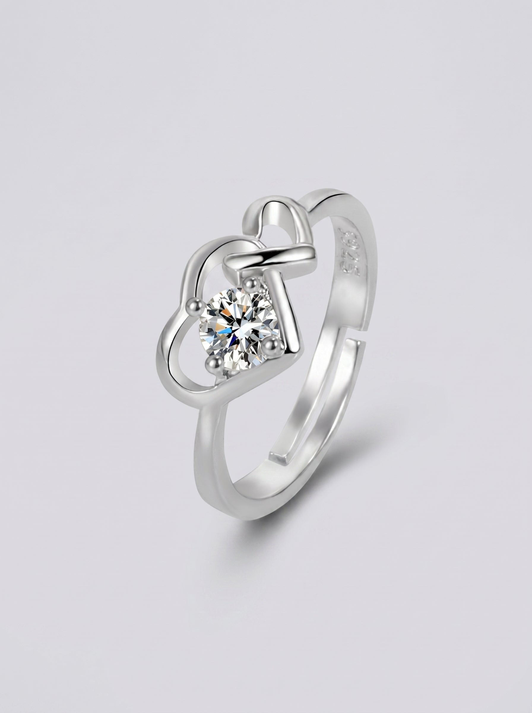 Anel em prata com um diamante em forma de coração sobre um fundo cinzento claro.
