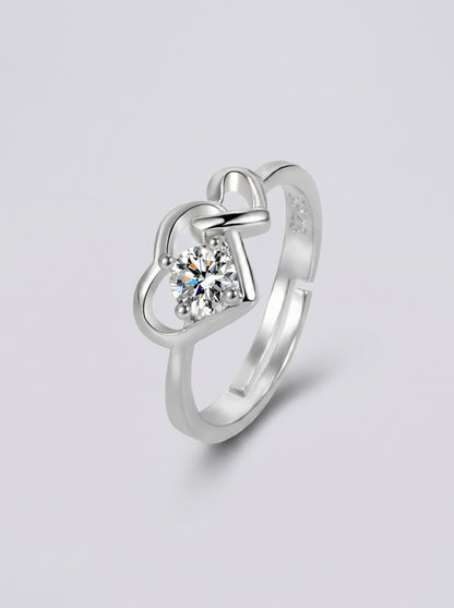 Anel em prata com um diamante em forma de coração sobre um fundo cinzento claro.
