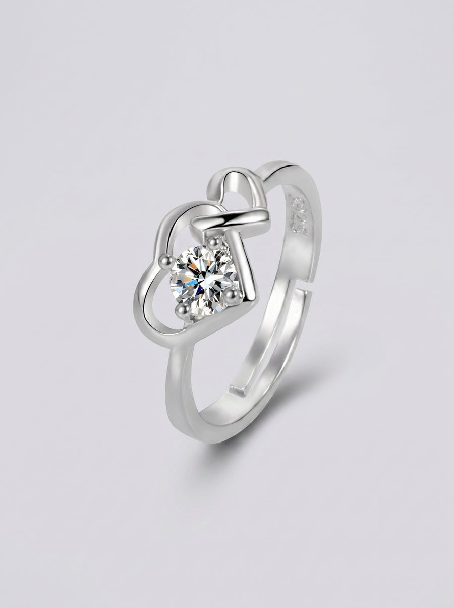 Anel em prata com um diamante em forma de coração sobre um fundo cinzento claro.
