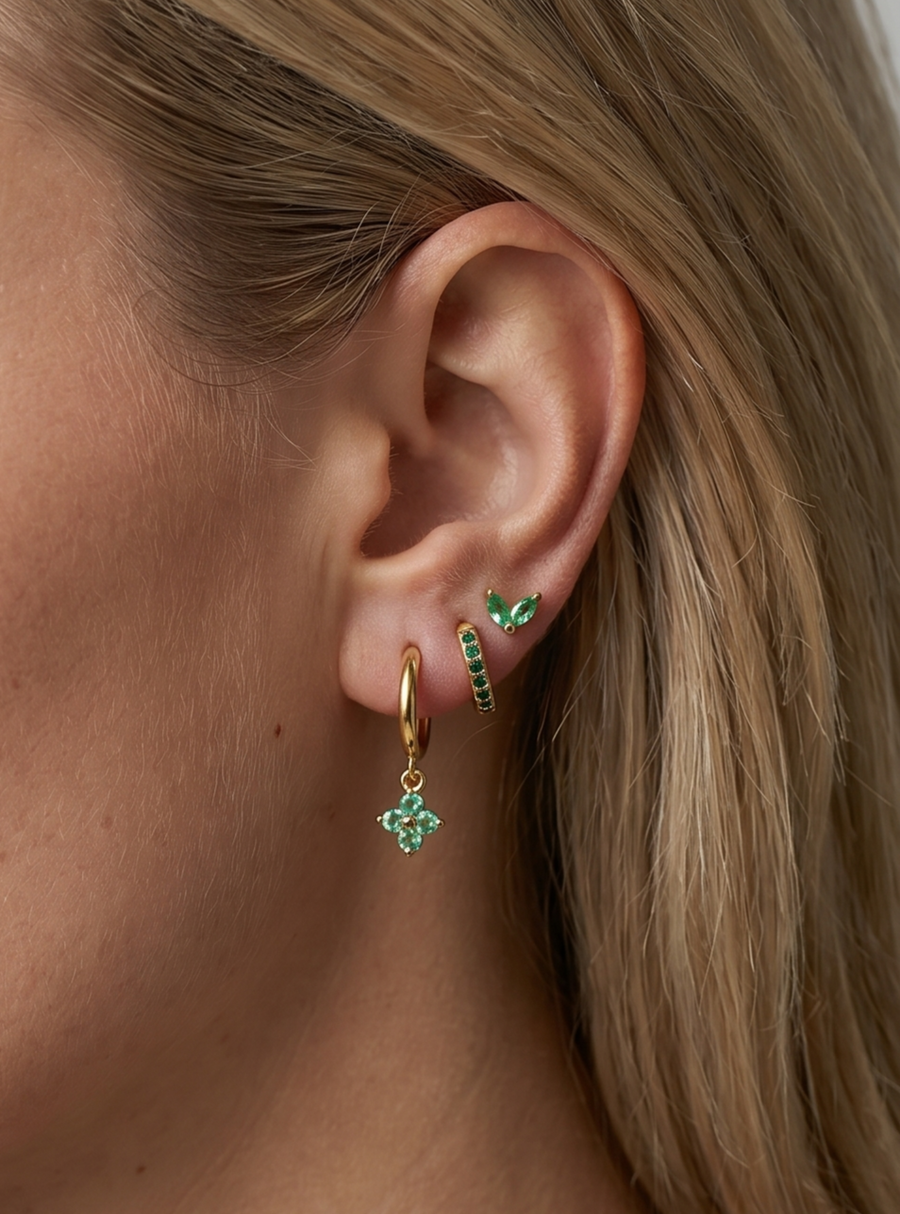 Brinco de argola dourado e brinco de pressão a combinar com detalhes em cristal verde, usados ​​na orelha da modelo para um look elegante.
