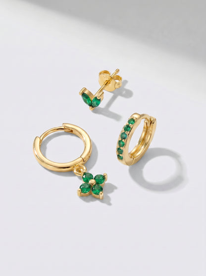 Brincos de argola e brincos de pino dourados com detalhes em cristal verde, fotografados sobre um fundo minimalista cinzento claro.
