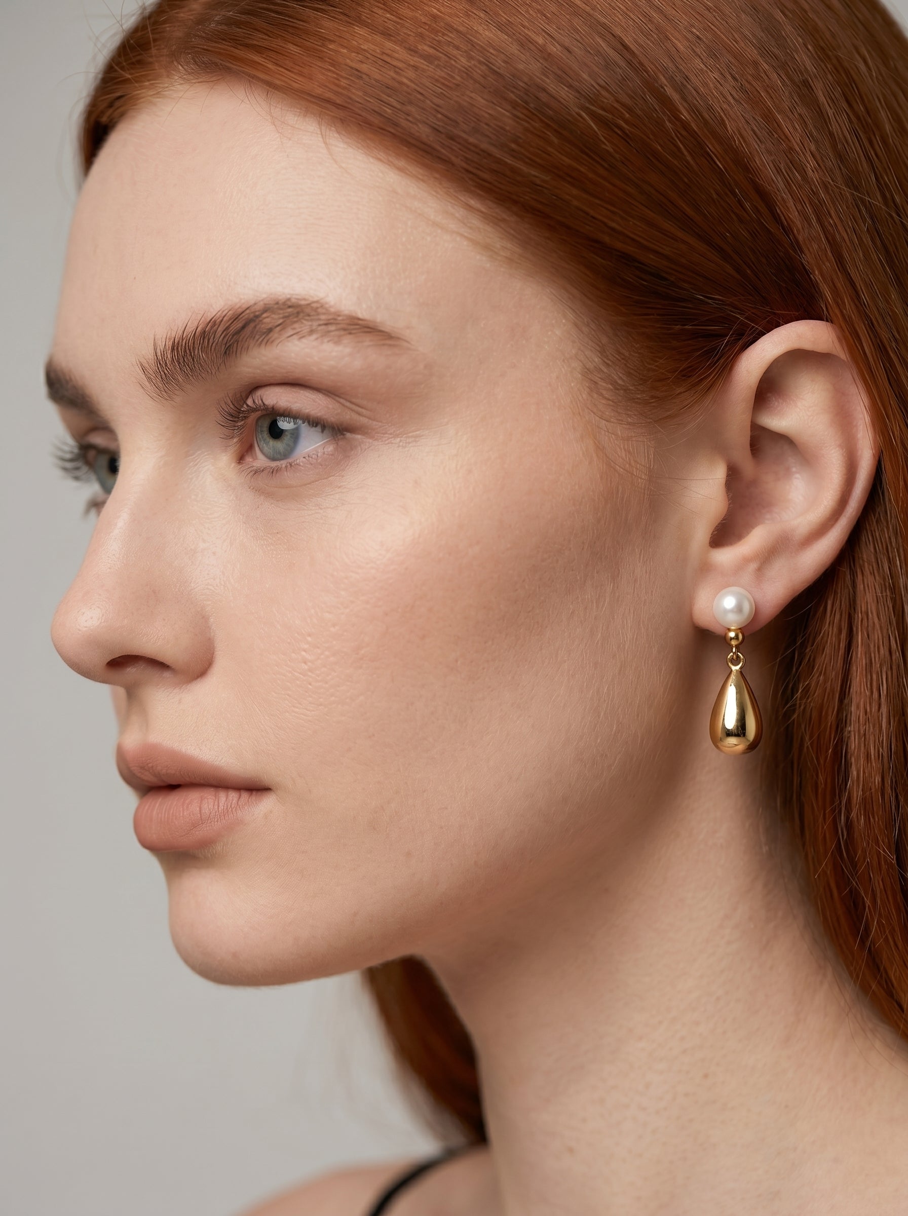 Brinco dourado pendente com pérola branca e gota metálica, usado por uma modelo para um visual elegante e sofisticado.