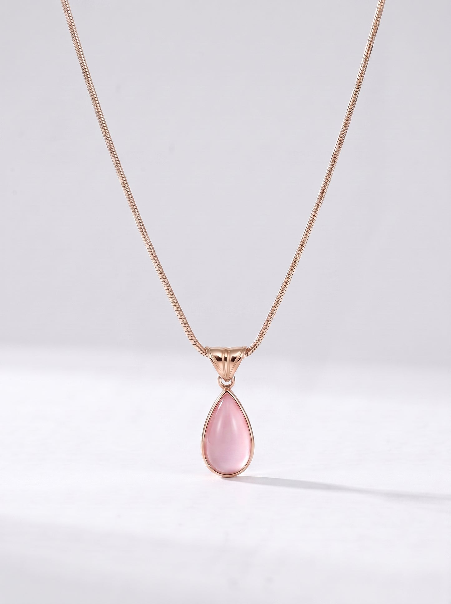 Colar dourado delicado com pendente rosa em forma de gota e acabamento elegante, fotografado sobre fundo claro para um visual feminino, sofisticado e delicado.