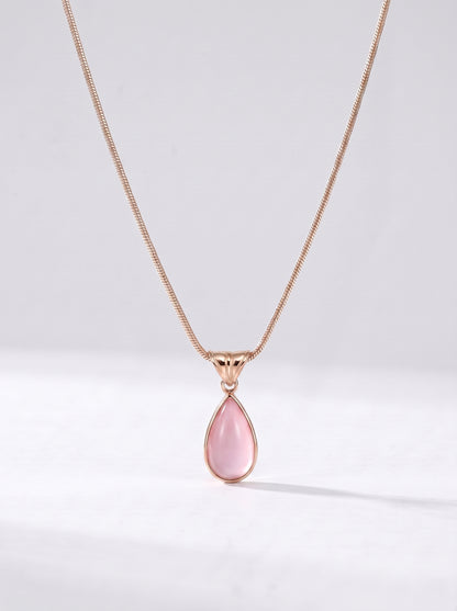 Colar dourado delicado com pendente rosa em forma de gota e acabamento elegante, fotografado sobre fundo claro para um visual feminino, sofisticado e delicado.