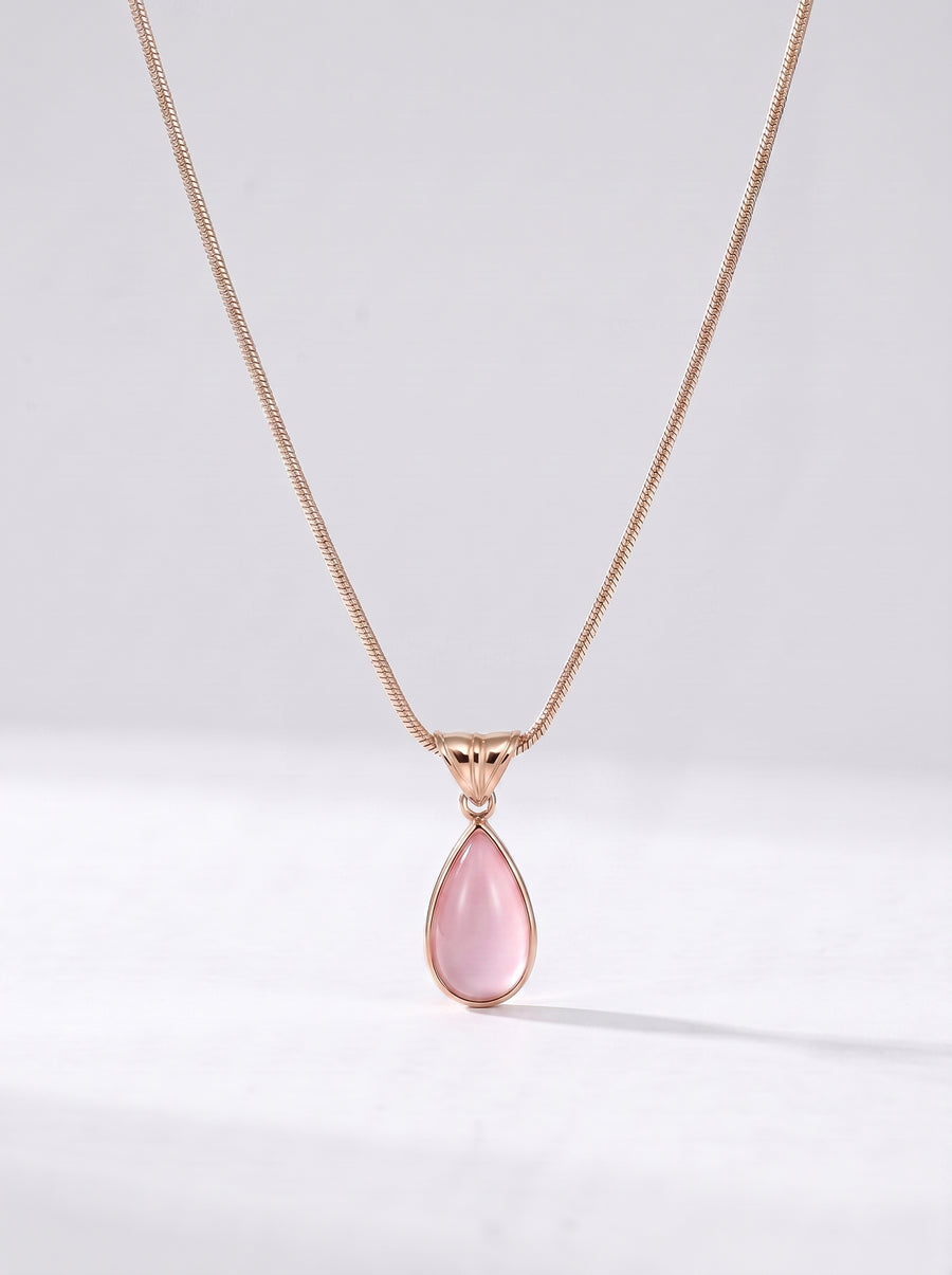 Colar dourado delicado com pendente rosa em forma de gota e acabamento elegante, fotografado sobre fundo claro para um visual feminino, sofisticado e delicado.