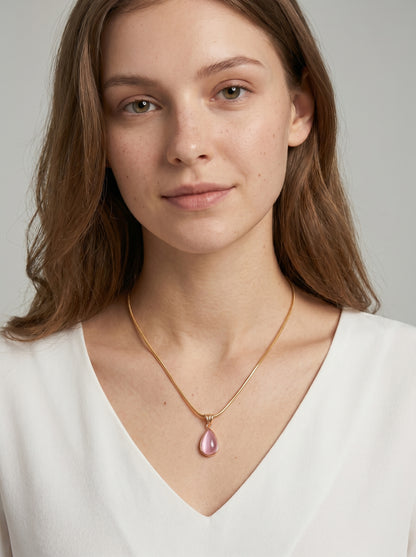 Colar dourado delicado com pendente rosa em forma de gota e acabamento elegante, usado por uma modelo para um visual feminino, sofisticado e delicado.