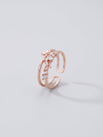 Anel aberto em ouro rosa com desenho floral sobre fundo cinza claro.
