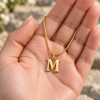 Colar personalizado dourado com inicial M apresentado na mão