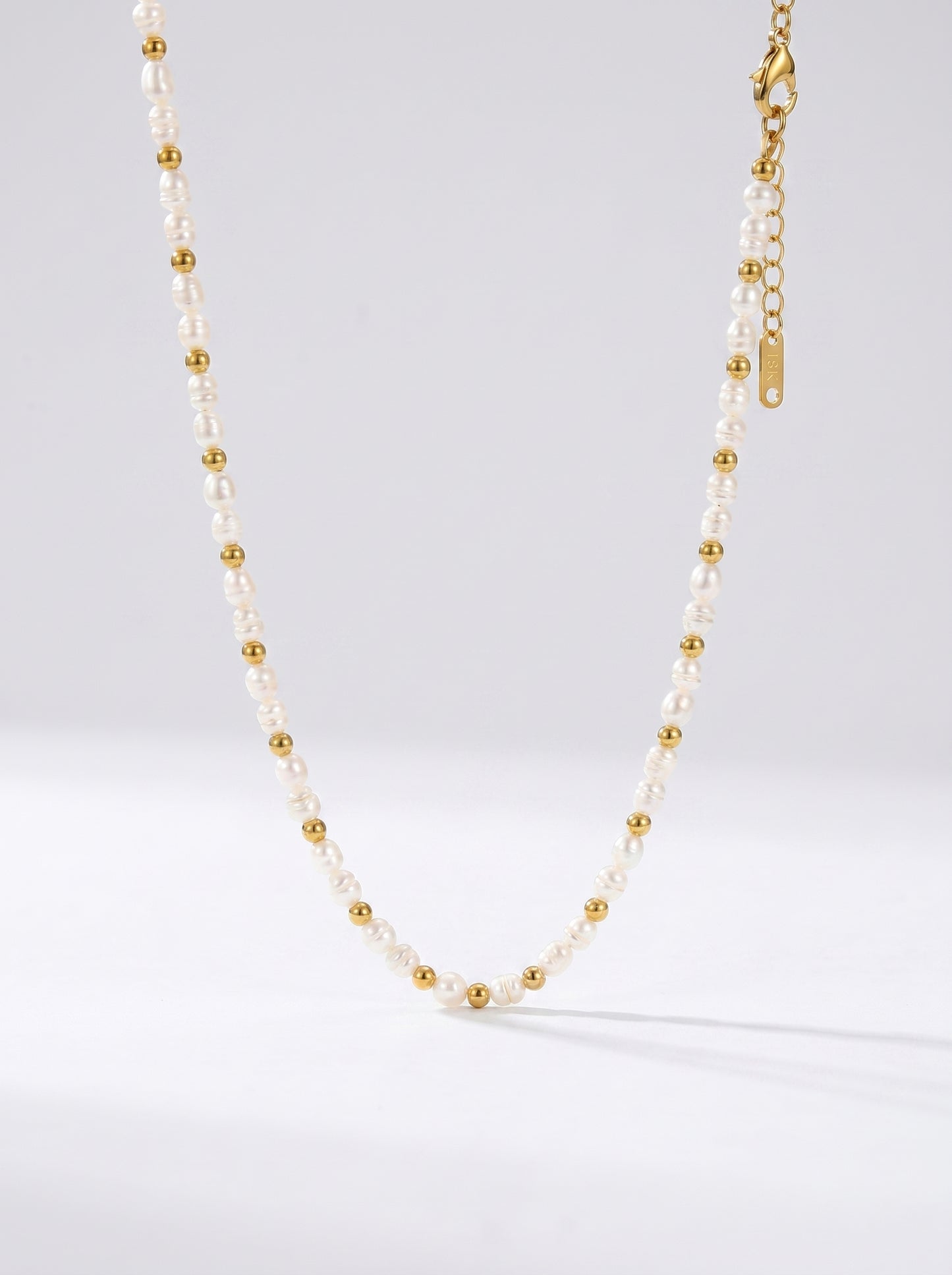 Colar delicado com pérolas brancas naturais e detalhes dourados, fotografado sobre fundo claro para um visual elegante, minimalista e sofisticado.