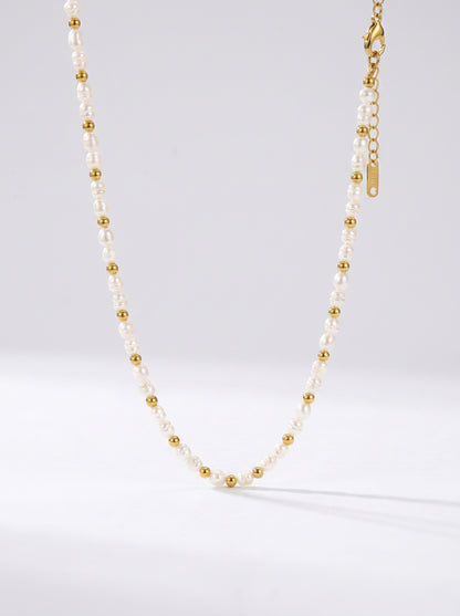 Colar delicado com pérolas brancas naturais e detalhes dourados, fotografado sobre fundo claro para um visual elegante, minimalista e sofisticado.