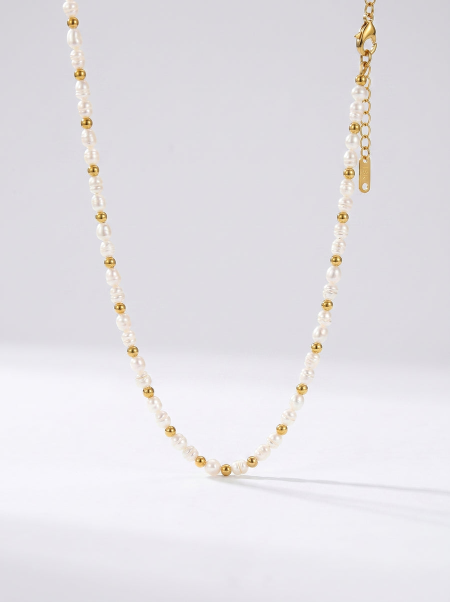 Colar delicado com pérolas brancas naturais e detalhes dourados, fotografado sobre fundo claro para um visual elegante, minimalista e sofisticado.