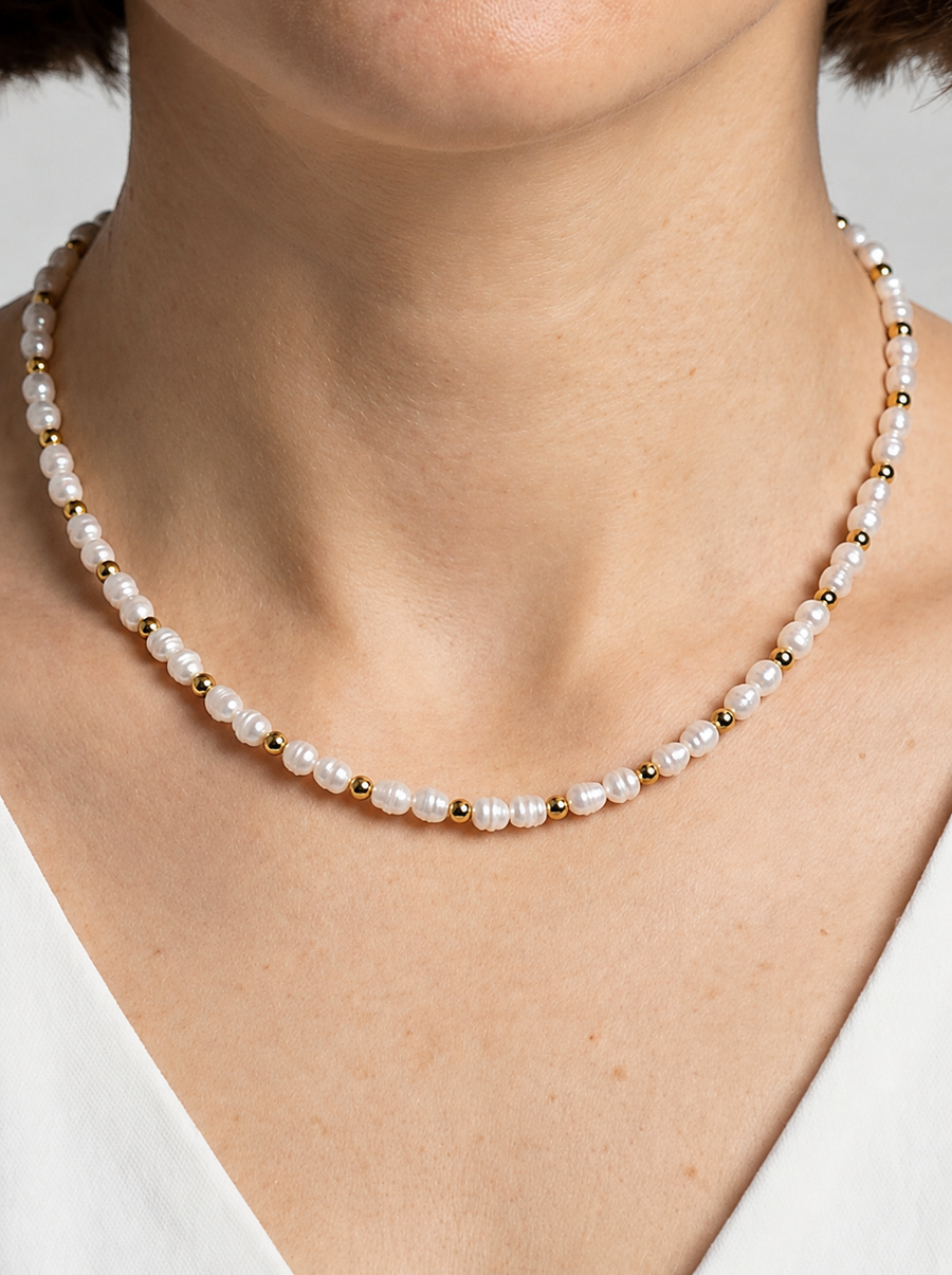 Colar delicado com pérolas brancas naturais e detalhes dourados, usado ao pescoço para um visual elegante, minimalista e sofisticado.