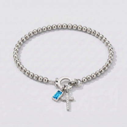 Pulseira prateada de contas com cruz e pedra de nascimento topázio azul de dezembro.