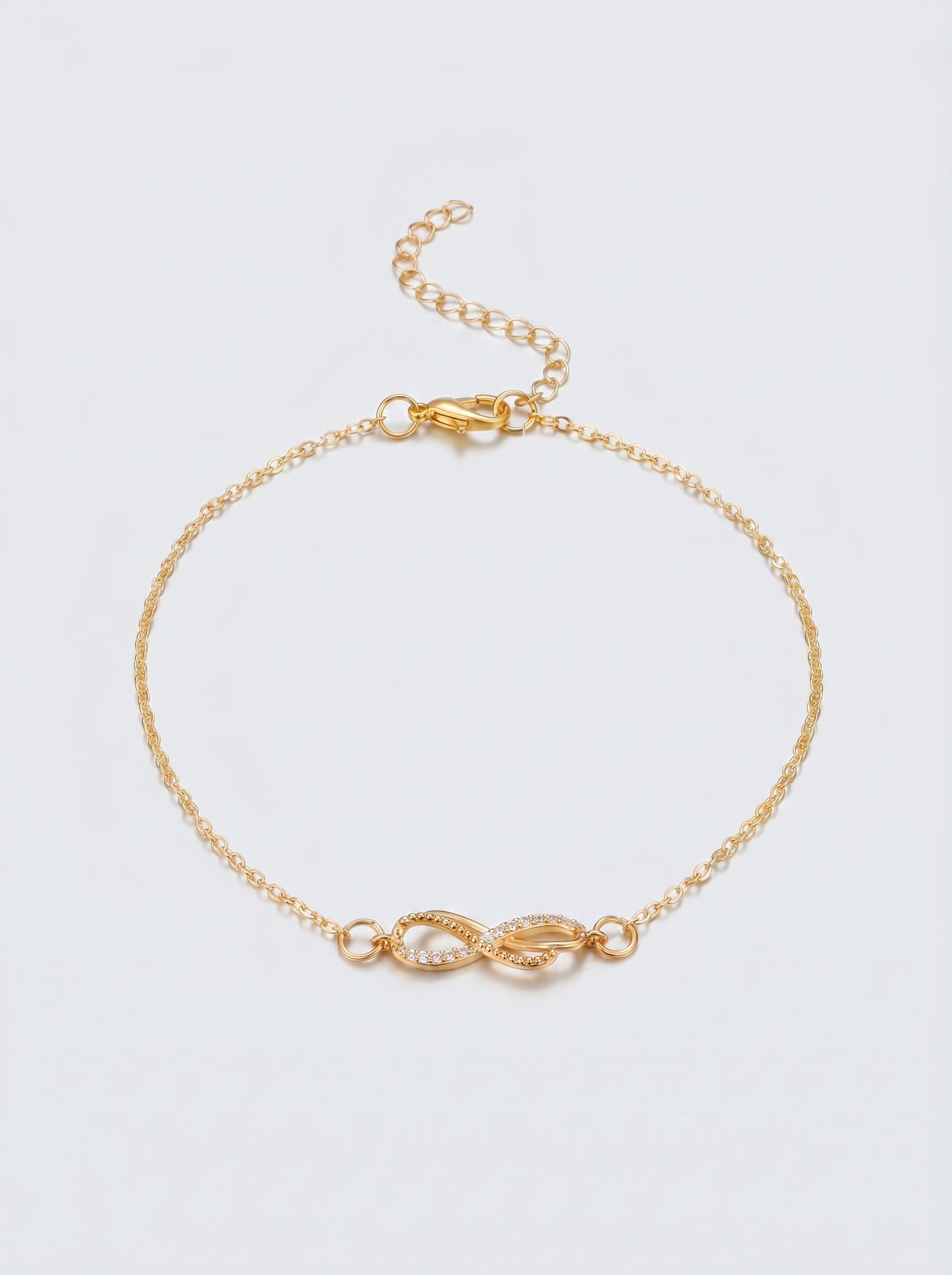 Pulseira dourada delicada com símbolo infinito e acabamento brilhante, fotografada sobre fundo claro para um visual elegante, feminino e minimalista.