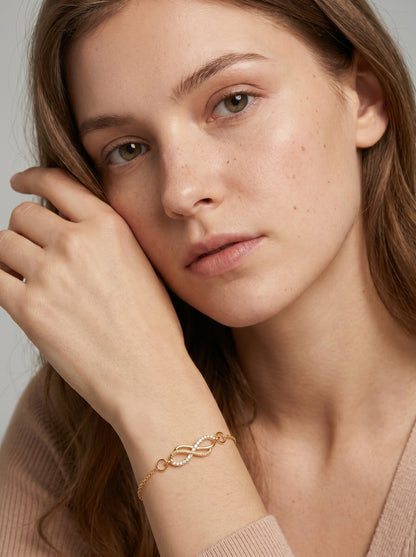 Pulseira dourada delicada com símbolo infinito, corrente fina e acabamento brilhante, usada por uma modelo para um visual elegante, feminino e minimalista.