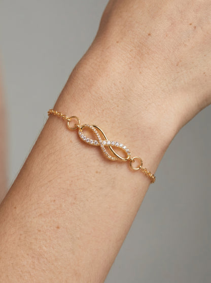 Pulseira dourada delicada com símbolo infinito, detalhe em cristais e corrente fina, usada no pulso para um visual elegante, feminino e minimalista.