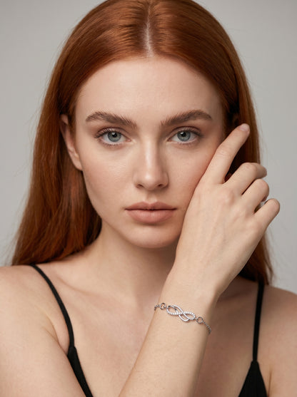 Pulseira prateada delicada com símbolo infinito, detalhe em cristais e corrente fina, usada por uma modelo para um visual elegante, feminino e minimalista.