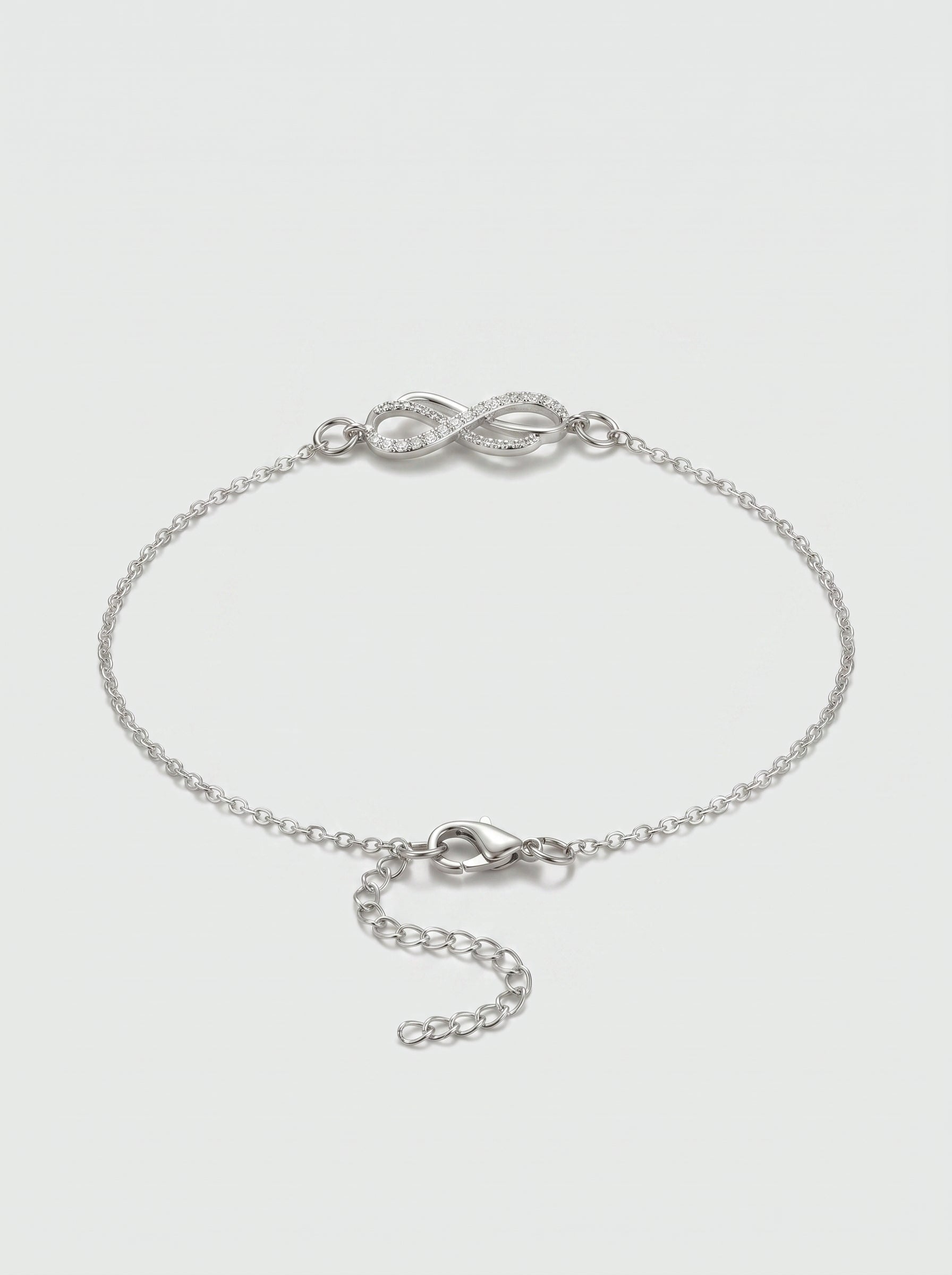 Pulseira prateada delicada com símbolo infinito, detalhe em cristais, corrente fina e fecho ajustável, fotografada sobre fundo claro para um visual elegante, feminino e minimalista.